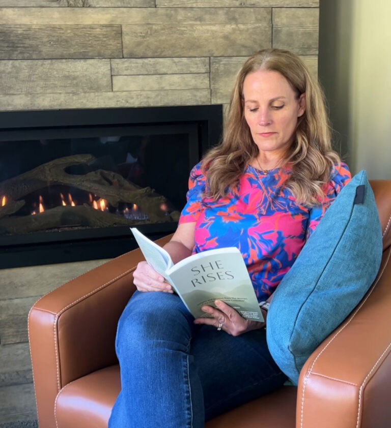 Angela Gaskin sitting in a leather chair next to the fireplace reading She Rises